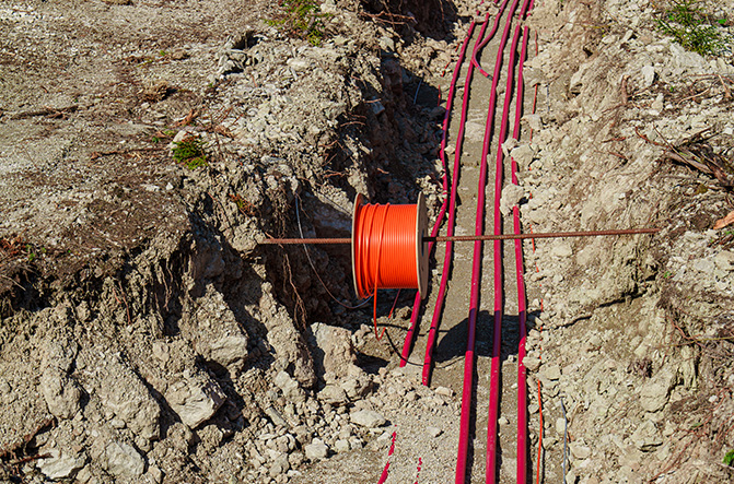 Vue détaillée d’une tranchée contenant plusieurs câbles rouges et une bobine de câble orange pour des travaux en basse ou haute tension