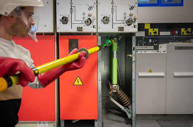 Technicien en formation HTA manipulant un dispositif haute tension avec une perche isolante dans un local électrique sécurisé