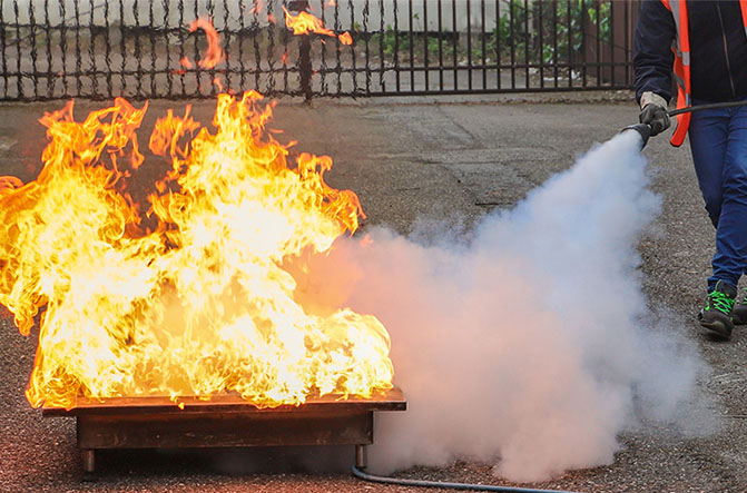 Formation mise en œuvre extincteurs : utilisation d’un extincteur sur un feu réel dans un bac à flammes simulé lors d’un exercice pratique