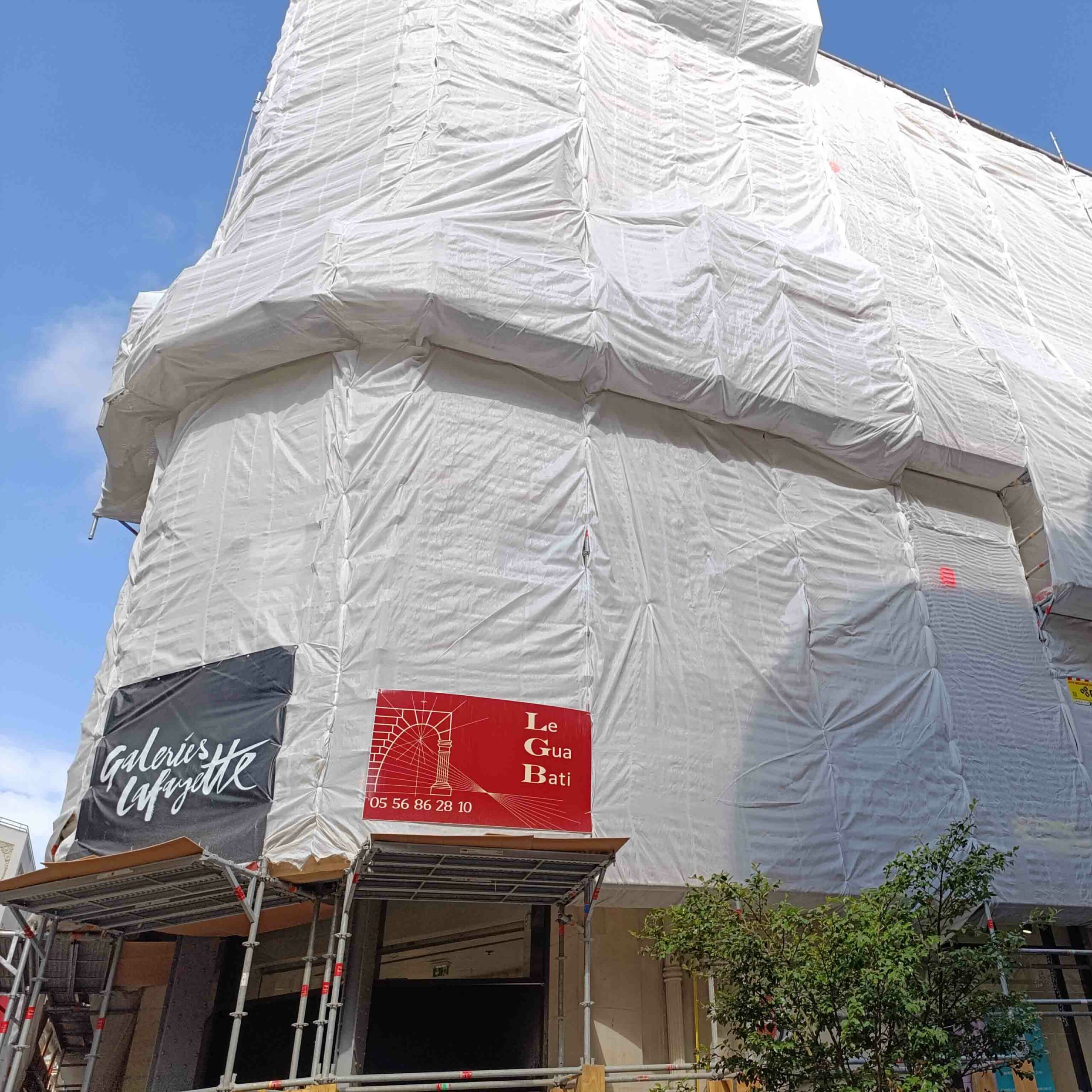Façade des Galeries Lafayette à Bordeaux recouverte de bâches pendant les travaux menés par Le Gua Bati
