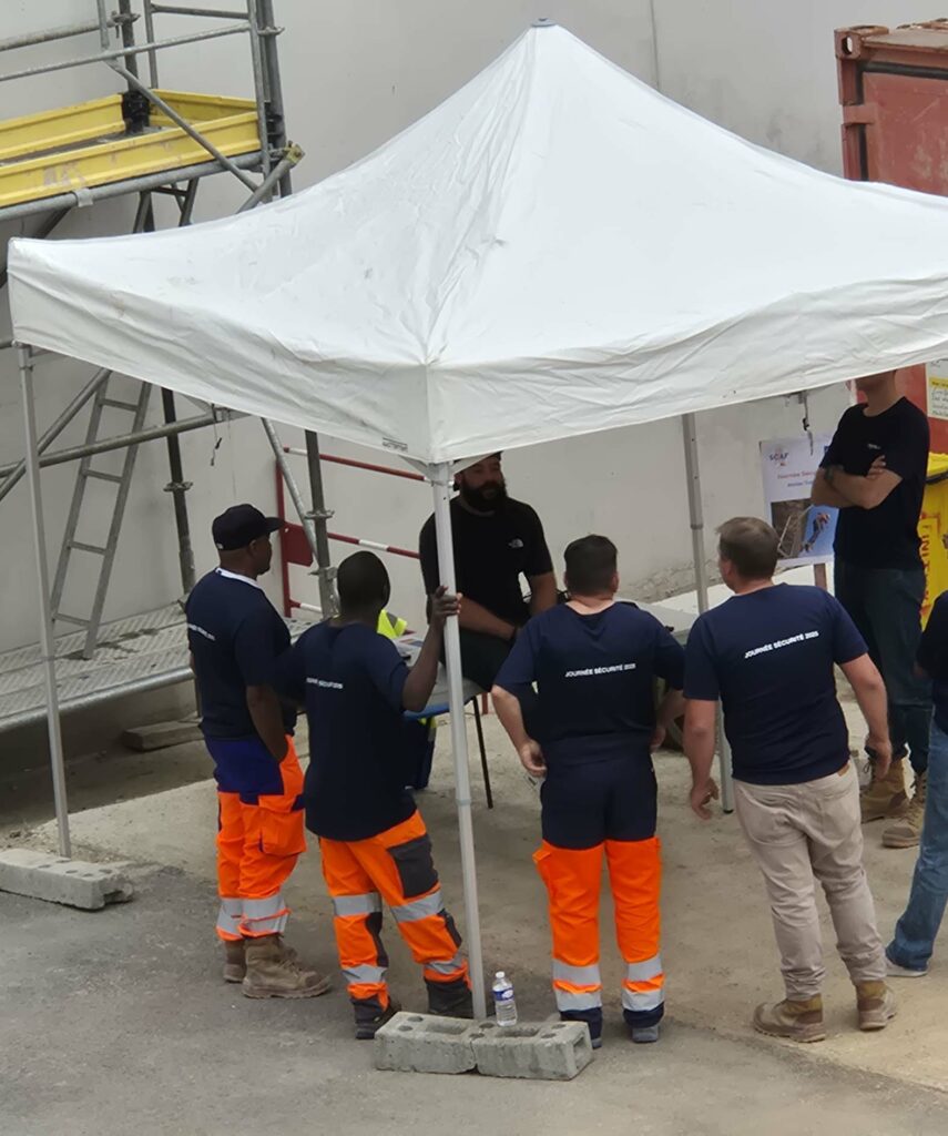 Groupe de collaborateurs en tenue de chantier réunis sous une tente pour un atelier de prévention des risques professionnels