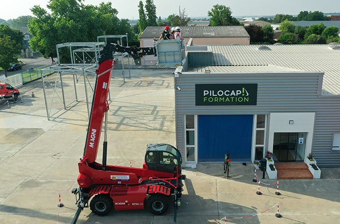 Formation travail en hauteur avec nacelle télescopique rouge devant le centre PILOCAP Formation, stagiaires encordés sur le toit