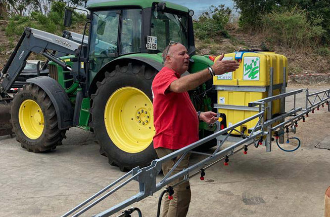 Formateur expliquant le fonctionnement d’un pulvérisateur agricole attelé à un tracteur lors d’une session de formation en plein air