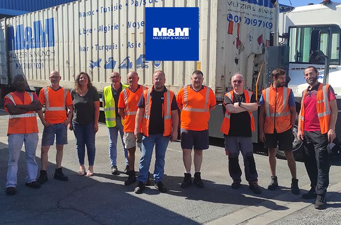Équipe logistique Militzer & Münch en tenue haute visibilité posant devant un conteneur de transport international