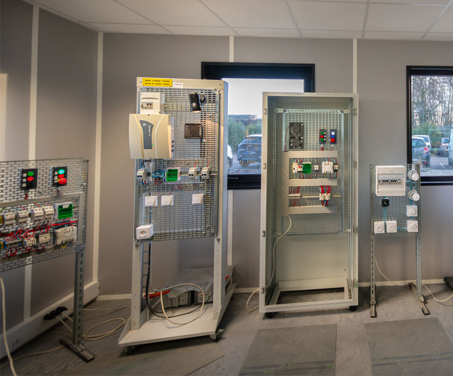 Photo d’un atelier pédagogique dédié à la formation en habilitation électrique BS BE manœuvre. On y voit plusieurs armoires et tableaux basse tension utilisés pour l’apprentissage des gestes de sécurité et des interventions sur installations électriques.