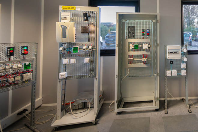 Photo d’un atelier pédagogique dédié à la formation en habilitation électrique BS BE manœuvre. On y voit plusieurs armoires et tableaux basse tension utilisés pour l’apprentissage des gestes de sécurité et des interventions sur installations électriques.