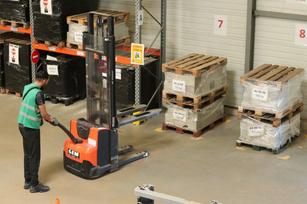 Cariste utilisant un gerbeur pour le stockage de charges lourdes sur palettes dans un rayonnage métallique industriel