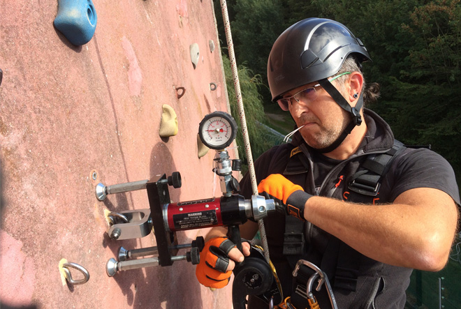 Technicien testant un point d’ancrage avec un dynamomètre sur une paroi, équipé d’un harnais et d’EPI pour le travail en hauteur