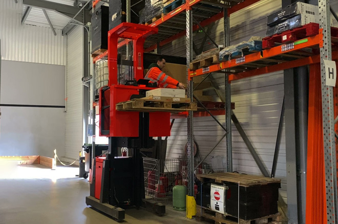 ariste équipé d’un gilet haute visibilité utilisant un chariot élévateur à poste de conduite élevable catégorie 6 pour le stockage de palettes en hauteur dans un entrepôt.