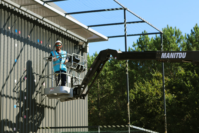 Opérateur équipé de harnais travaillant en hauteur sur une nacelle élévatrice Manitou le long d’un bâtiment industriel
