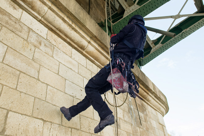 Technicien cordiste effectuant des travaux en hauteur sous un pont métallique