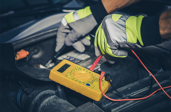 Opérateur mesurant avec un multimètre la tension d'une batterie électrique de véhicule