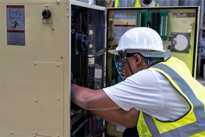 Technicien en gilet haute visibilité et casque blanc intervenant sur une armoire électrique ouverte